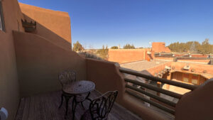 Private rooftop balcony with wrought iron table and chairs overlooking traditional adobe architecture and scenic desert landscape at The Zia Apartment.