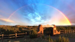 A stunning rainbow arcs over The Chi Center entrance, surrounded by serene natural landscapes and vibrant skies, symbolizing peace and healing.