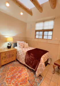 Cozy guest room at The Serenity Center with rustic beams, warm lighting, and inviting bed with burgundy accents, creating a peaceful retreat.