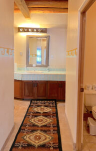 Serenity Center bathroom featuring a colorful Southwestern-style rug, tiled countertop with double sinks, wooden cabinetry, and a mirror reflecting soft natural light.