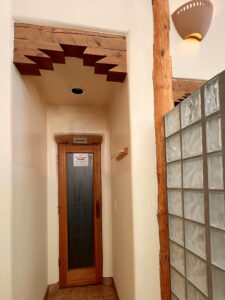 Entrance to the Serenity Center Sauna, featuring a wooden door with frosted glass, surrounded by natural wood accents and adjacent to a frosted glass wall for a calming and rejuvenating ambiance.