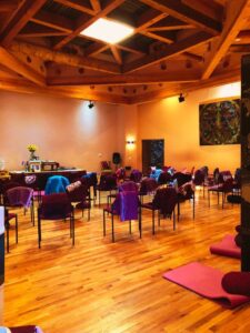 Interior view of the Sacred Space at The Chi Center, featuring warm wooden floors, vibrant chairs, and a tranquil ambiance designed for meditation, healing, and community gatherings.