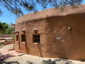 Exterior view of The Kiva at The Chi Center, showcasing traditional adobe architecture and serene surroundings under a bright blue sky.
