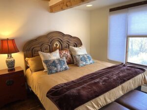 Zia Master Bedroom featuring a handcrafted wooden headboard with intricate details, soft ambient lighting, and a serene window view with natural light streaming through.
