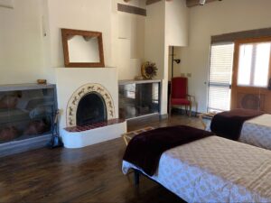 Main Lodge #8 - SPIRAL room at The Chi Center featuring twin beds with cozy bedding, a traditional kiva fireplace adorned with spiral petroglyph designs, polished wood floors, and a serene ambiance for a restful stay.