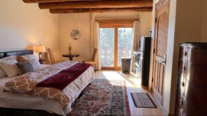 Spacious Pueblo House #7 - SANDIA room at The Chi Center, featuring a king-size bed with cozy linens, a private balcony with serene views, a dining nook, natural wood accents, and ample natural light for a tranquil retreat