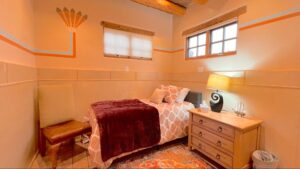 Serenity Center #4 - WISDOM room at The Chi Center, showcasing a comfortable twin bed with elegant bedding, warm lighting, natural wood accents, and artistic wall designs for a tranquil and reflective retreat experience.