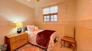 Serenity Center #3 - ALCHEMY room at The Chi Center featuring a cozy twin bed with elegant bedding, southwestern-inspired wall art, warm wooden furniture, and a serene atmosphere for relaxation and reflection.