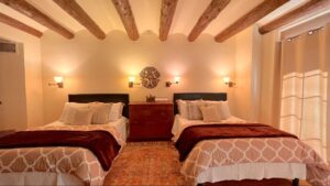 "Serene Pueblo House #4 - HOPI room at The Chi Center, featuring two double beds with elegant bedding, warm lighting, natural wood ceiling beams, and tranquil decor for a rejuvenating stay.