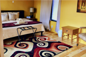 Cozy and inviting loft room featuring a plush bed with vibrant bedding, a colorful spiral-patterned rug, wooden floors, and charming furniture in Loft Room #3.
