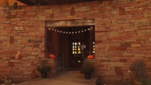 Entrance to a rustic building with a stone facade, decorated with hanging chili ristras, pumpkins, and potted plants, creating a warm and inviting atmosphere for a reception area.