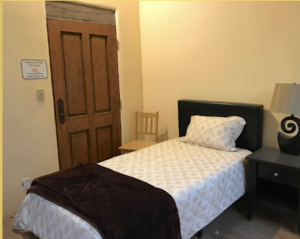 Cozy bedroom in Main Lodge #5 - FATHER SKY, featuring a single bed with a patterned comforter, a wooden door, a chair, and a bedside table with a decorative lamp, creating a warm and inviting retreat atmosphere.