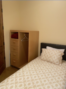 Cozy bedroom in Main Lodge #3 - THE COOK'S NOOK, featuring a single bed with a patterned comforter, a wooden wardrobe with drawers, and a simple, minimalist design for a comfortable retreat experience.