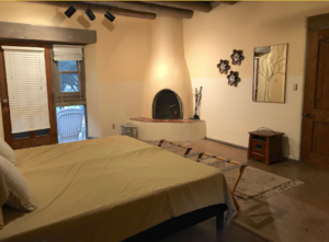 Spacious bedroom in Main Lodge #1 - VISION QUEST, featuring a comfortable bed with yellow bedding, a cozy corner fireplace, artistic wall decor, and a door leading to an outdoor patio area, creating a warm and inviting retreat atmosphere