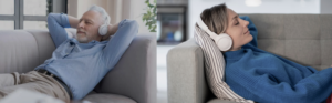 Relaxed elderly man and woman wearing headphones, lying comfortably on couches, enjoying a meditative or calming audio experience at home.