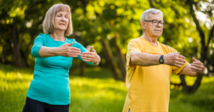 Senior couple practicing Qigong in a peaceful park setting, performing gentle energy-balancing movements to promote health, relaxation, and vitality.