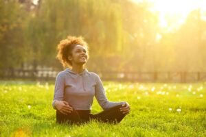 Young woman with curly hair joyfully practicing Qigong in a sunlit meadow, exemplifying life mastery