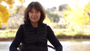Portrait of a woman speaking outdoors against a backdrop of vibrant autumn foliage, conveying a serene and reflective atmosphere.