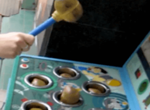 Close-up of a Whac-A-Mole arcade game with a mallet striking one of the moles, symbolizing quick reflexes and playful fun.