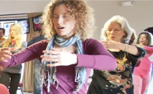 Group of individuals practicing Qigong with focused expressions, gentle hand movements, and a serene atmosphere in a softly lit room.