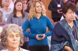 "Group of individuals meditating with eyes closed, hands resting in a relaxed mudra, creating a calm and focused atmosphere during a group practice session.
