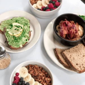 Delicious breakfast spread featuring avocado toast with lemon, granola bowls topped with fresh berries and bananas, creamy oatmeal with crispy bacon, and slices of whole-grain bread.