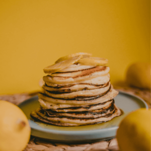 Stack of fluffy pancakes topped with caramelized lemon slices, served on a blue plate with a vibrant yellow background for a cheerful breakfast setting.