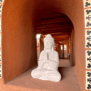 Serene white Buddha statue in a meditative pose, nestled within an adobe alcove adorned with intricate tile accents, illuminated by warm natural light.