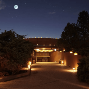 Tranquil nighttime view of The Chi Center illuminated pathway leading to an adobe-style sanctuary, under a starry sky and glowing full moon.