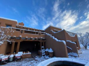 Southwest-style adobe building covered in a light blanket of snow under a clear blue sky, showcasing the beauty of winter in a serene desert setting