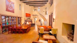 Warm and inviting interior of a Southwest-style sanctuary featuring a dining table, cozy seating area, fireplace, and curved staircase with artistic decor and natural lighting.