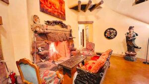 Cozy Southwest-style living area with a stone fireplace, intricately carved wooden furniture, colorful cushions, and a statue of a serene figure in the corner, creating a warm and inviting atmosphere.