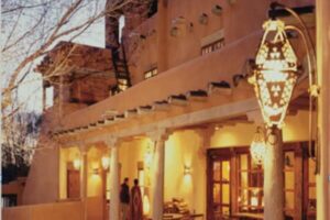 Exterior of an adobe-style building illuminated by warm lanterns at dusk, showcasing traditional Southwestern architecture with wooden beams and a cozy, inviting atmosphere.