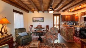 Cozy Southwestern-style living room and kitchen with rustic wooden beams, elegant furnishings, and vibrant rugs creating a warm, inviting atmosphere.
