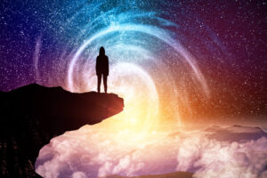 Silhouette of a person standing on the edge of a cliff, gazing into a vibrant cosmic vortex of swirling stars, with clouds and mountain peaks in the distance.