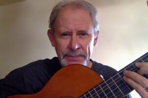 Chris Harrell holding a classical guitar, looking directly at the camera with a neutral background.
