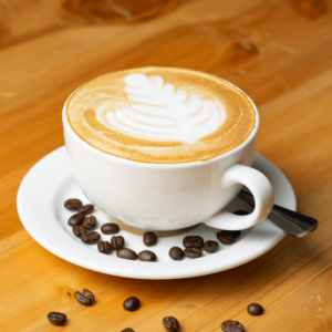 Latte art in a white coffee cup on a saucer, surrounded by scattered coffee beans on a wooden table.