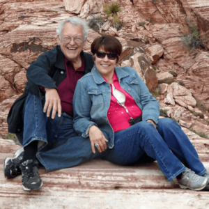 Rick and Judy smiling while seated on striking red rock formations, enjoying a moment of connection and natural beauty in an outdoor setting.