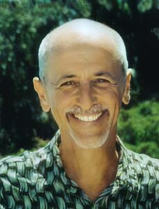 Smiling portrait of Brian Bouch in a patterned shirt, with a natural green outdoor background.