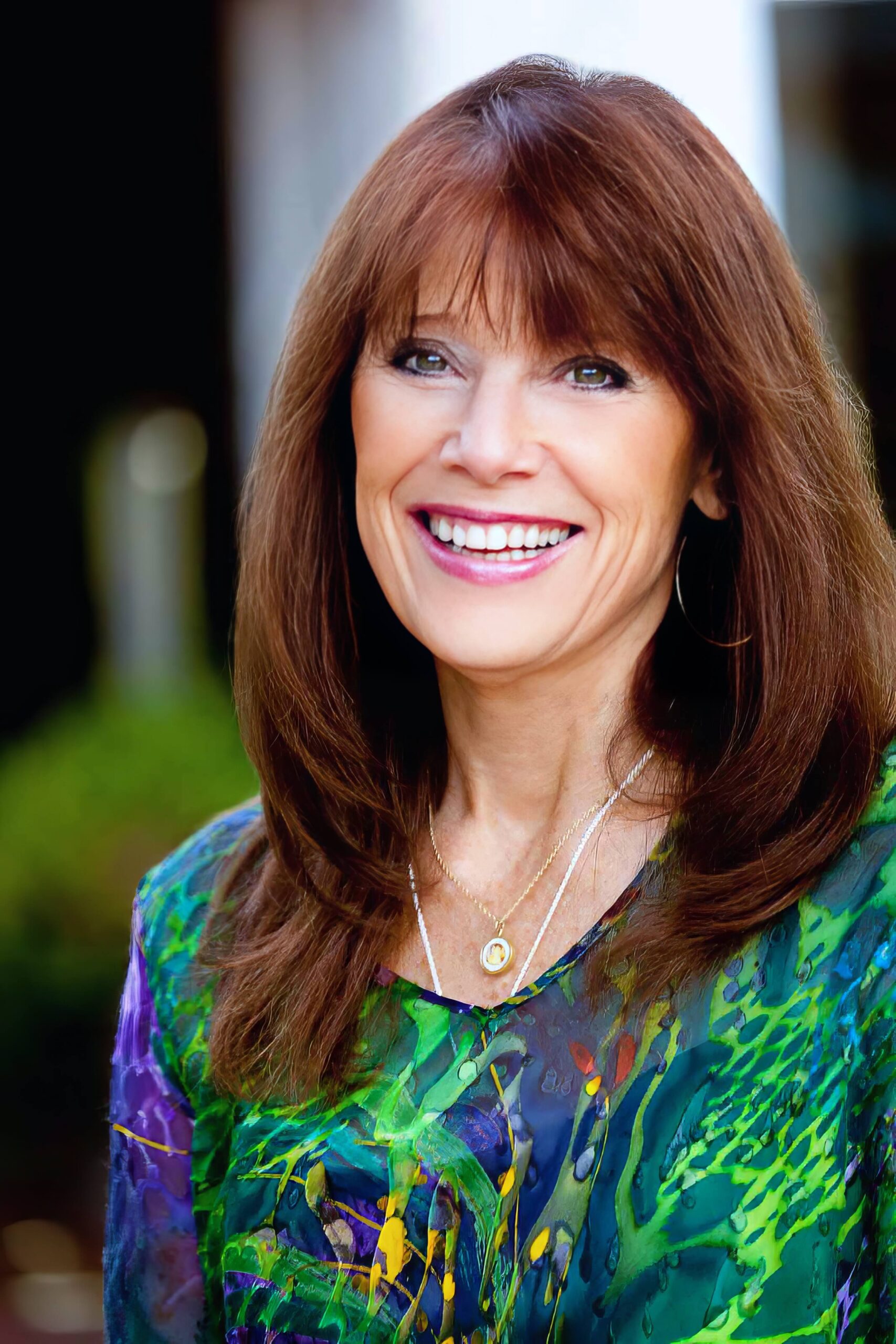 Janet Bray Attwood smiling brightly, with auburn hair and wearing a vibrant green and purple patterned blouse.