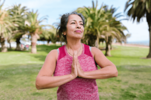 Confident woman practicing mindfulness and gratitude outdoors, surrounded by lush green palm trees in a serene park setting.