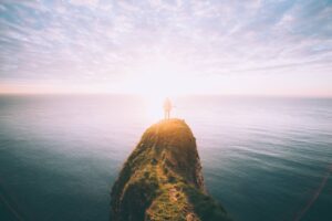A lone figure stands at the edge of a grassy cliff overlooking an expansive ocean, bathed in soft sunlight, symbolizing self-discovery, reflection, and limitless potential."