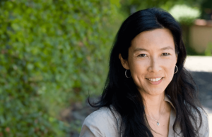 Cynthia smiles warmly against a lush green backdrop, reflecting serenity and inner peace from her transformative experience with Wisdom Healing Qigong.