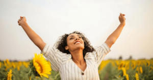 A joyful woman stands in a sunflower field with her arms raised towards the sky, embodying a sense of freedom, connection, and inner peace, capturing the essence of the Connections series.