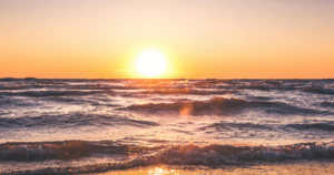 Sunset over the ocean, radiating source energy as captured in a serene Wisdom Healing Qigong practice, reflecting the principles of Hun Yuan Chi and sound healing. The sun dips low, casting a brilliant orange glow across the choppy sea waves, embodying a moment of natural harmony and tranquility.