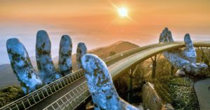 The Golden Bridge in Vietnam, held aloft by two giant stone hands, at sunrise. This iconic bridge symbolizes strength and support, mirroring themes of self-love and spirituality in Wisdom Healing Qigong. The warm sunlight bathing the scene enhances feelings of health and well-being, capturing a moment of peace and contemplation.