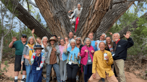 Joyful group gathered around the majestic Grandmother Tree on Magical Sunday, with participants smiling, waving, and embracing the natural setting, symbolizing unity and celebration of nature’s beauty.