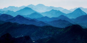 A breathtaking view of layered mountain ranges fading into the distance, painted in shades of deep blue and green. The atmospheric perspective creates a serene and mystical effect, inviting a sense of tranquility and introspection. This expansive, natural landscape perfectly captures the peaceful and contemplative spirit of the 2024 Fall Retreats.