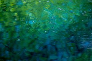 A close-up of gently rippling water in vibrant shades of green and blue, with small bubbles forming on the surface. The calming movement and rich colors evoke a sense of serenity and natural beauty, symbolizing tranquility and renewal. This image captures the essence of relaxation and reflection central to the 2024 Fall Retreats.