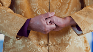 Close-up of hands in a traditional Qigong gesture, clasped together with a sense of calm focus, wearing a golden garment adorned with intricate patterns, symbolizing unity, balance, and inner strength in the journey of health and spiritual growth.